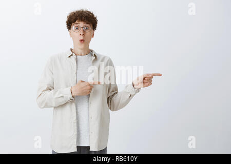 Prezzi Incredibple diritto su angolo. Ritratto di impressionato incuriosito e senza parole simpatico tizio in bicchieri con capelli ricci la piegatura delle labbra e spuntano gli occhi dallo stupore come rivolto a spazio di copia Foto Stock