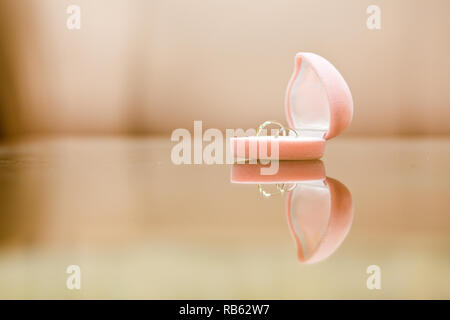 Gli anelli di nozze in un rosa portagioie sulla superficie dello specchio Foto Stock