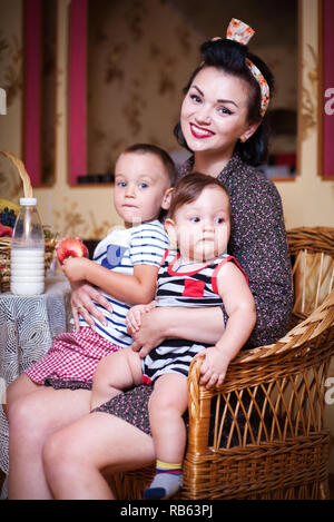 Ritratto di madre e due figli all'interno della cucina, girato in stile retrò. Studio shot, arredamento. Foto Stock