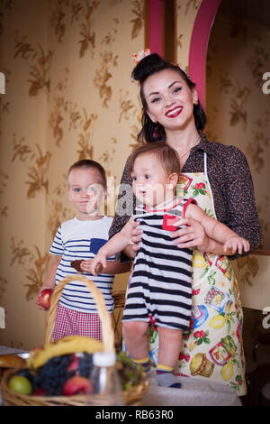 Ritratto di madre e due figli all'interno della cucina, girato in stile retrò. Studio shot, arredamento. Foto Stock