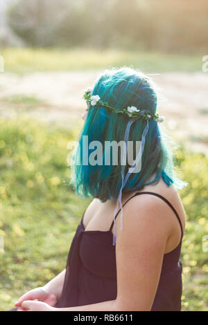 Una ragazza di sedersi su un parco con capelli blu e una corona di fiori e vestito nero Foto Stock