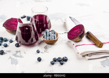 Barbabietola fresca e succo di mirtillo su bianco sullo sfondo di legno. Spazio di copia Foto Stock