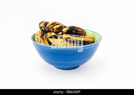 Un mazzetto di molto surmature le banane in un blu e verde vaso in ceramica isolata su uno sfondo bianco Foto Stock