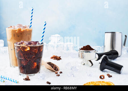 Estate bere caffè ghiacciato in un bicchiere di ghiaccio e caffè con la crema in un bicchiere alto circondato da ghiaccio, chicchi di caffè, portafilter, antimanomissione bricco per latte e vario Foto Stock