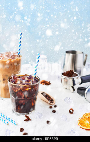 Inverno bere caffè ghiacciato in un bicchiere di ghiaccio e caffè con la crema in un bicchiere alto circondato da ghiaccio, chicchi di caffè, portafilter, antimanomissione bricco per latte e vario Foto Stock