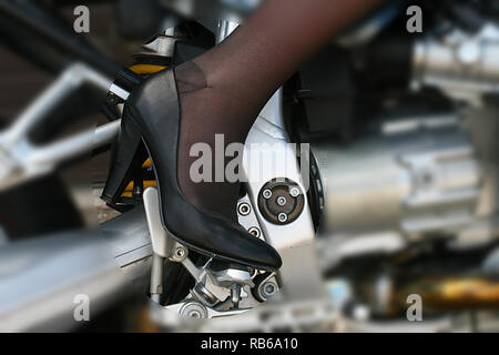 Donna bionda che indossa calza in nylon, tacchi alti e pantaloncini corti in sella a una motocicletta Foto Stock