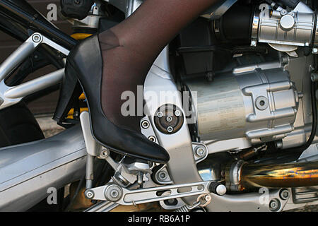 Donna bionda che indossa calza in nylon, tacchi alti e pantaloncini corti in sella a una motocicletta Foto Stock