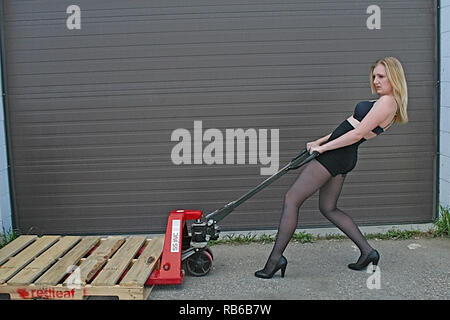 Donna bionda che indossa calza in nylon, tacchi alti e brevi spingendo una ruota barrow Foto Stock