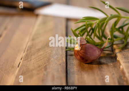 Spicchio di aglio su un rustico in legno bordo. Bianco di ceramica di coltello fuori di immagine da dietro. Foto Stock