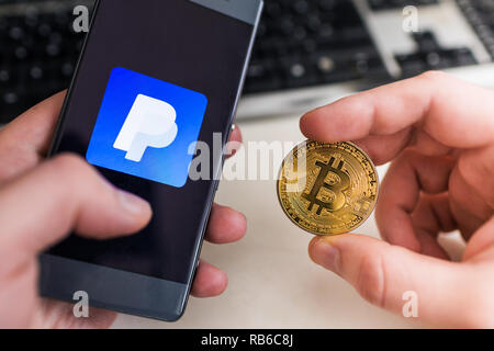 SLOVENIA - Gennaio 8, 2019: uomo azienda Bitcoin monete e in altri smartphone a mano con applicazione di Paypal. Foto Stock