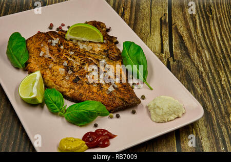 Fried rainbow-Bistecca al pepe con pepe, sale, senape e ketchup, guarnite con foglie di basilico e pezzi di calce, servita su un piatto di rosa. Appartamento , horizo Foto Stock