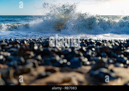 Paesaggio fotografia scattata da basso punto di vista su di un fuoco sulla spiaggia di ghiaia con un onda di schiantarsi in-fuoco in background. Foto Stock