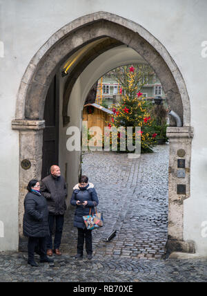 Compagnia di persone in attesa nel medioevo ingresso ad arco al Bischofshof Hotel in Regensburg. Un albero di Natale può essere visto nel cortile al di là. Foto Stock