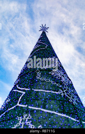 Fotografia a colori della conica grande albero di Natale decorato con una stella d'argento e blu e luci bianche prese dal di sotto. Foto Stock