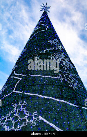 Fotografia a colori della conica grande albero di Natale decorato con una stella d'argento e blu e luci bianche prese dal di sotto. Foto Stock