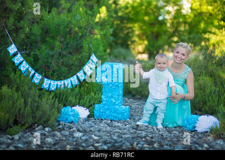 Bellissima madre lady mom in elegante vestito blu insieme con il suo figlio e il numero di un compleanno nel parco. Foto Stock