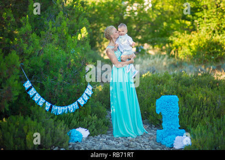 Bellissima madre lady mom in elegante vestito blu insieme con il suo figlio e il numero di un compleanno nel parco. Foto Stock