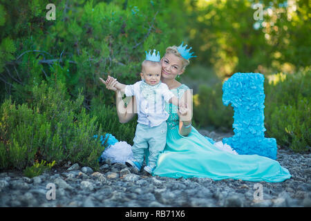 Bellissima madre lady mom in elegante vestito blu insieme con il suo figlio e il numero di un compleanno nel parco. Foto Stock