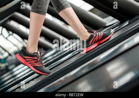 Giovane donna in palestra uno stile di vita sano camminando sul tapis roulant gambe indossando sneakers close-up Foto Stock