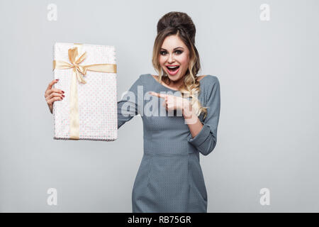 Ritratto di soddisfatto bella giovane donna in uno stile informale e permanente di puntare il dito a presentare con giallo di prua e sorriso toothy, guardando camer Foto Stock