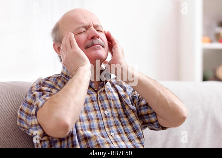 Senior uomo con i baffi con un mal di testa a casa. Terribile concetto di emicrania. Foto Stock
