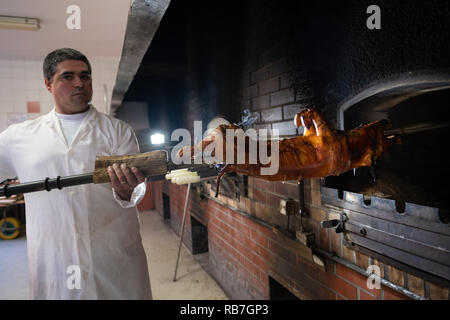 L'uomo prendendo un maialino fuori del forno dove è stato arrostito in Portoghese tradizionale regione di Bairrada, Mealhada, Portogallo Foto Stock