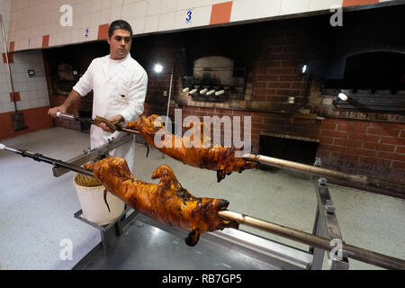L'uomo tenendo un maialino allo spiedo che veniva tostata in Portoghese tradizionale regione di Bairrada, Mealhada, Portogallo Foto Stock