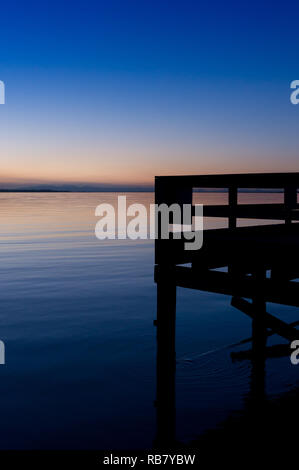 Silhouette di pier si affaccia la calma acqua oceanica in ingresso alla baia di fango al crepuscolo. Spiaggia a mezzaluna, Surrey, British Columbia, Canada. Foto Stock