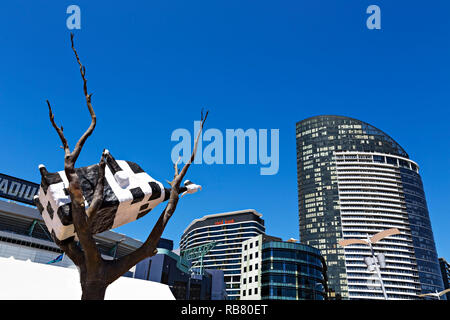 La vacca su un albero di una scultura in Melbourne Docklands.Il punto di Victoria Apartments,Medibank costruzione,e Bendigo Bank può essere visto in background. Foto Stock