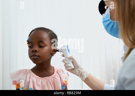 Ritratto di adorabile bambina in abito rosa in seduta medici ufficio. Ragazza carina in attesa che guarda lontano mentre infermiera professionale e di lavoro il trattamento di lei. Concetto di assistenza sanitaria. Foto Stock