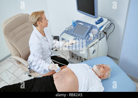 Vista superiore del medico osservando il paziente con moderne attrezzature mediche in esame alcuni problemi. senior uomo posa sul letto e la consultazione con il medico professionale. Donna che guarda la schermata di lavoro e. Foto Stock