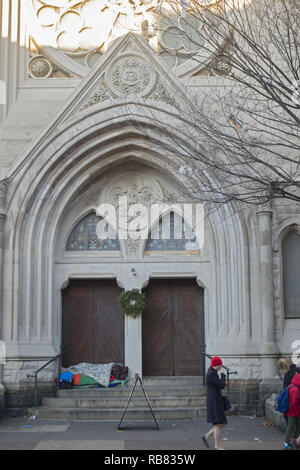 Persona senzatetto dorme sui gradini di una chiesa lungo la 7th Avenue a Park Slope, Brooklyn durante la stagione di festa di Natale. Foto Stock