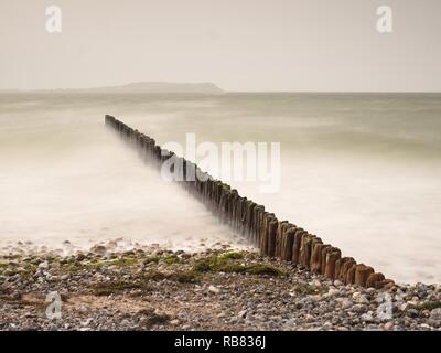 Le onde in arrivo colpendo vintage legno vecchio presso la costa. Una lunga esposizione al tramonto di pier palificazioni Foto Stock