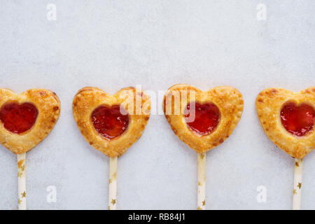 A forma di cuore pop a torta con confettura di fragole. In casa biscotti frollini su un bastone per il giorno di San Valentino. Foto Stock