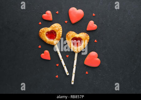 Torta alle fragole pop su un bastone per il giorno di San Valentino. A forma di cuore smaltato rosso i cookie. Vista superiore Foto Stock