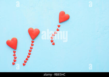 Cuore rosso palloncini sagomati realizzati di cookie e di candy fly out. Il giorno di San Valentino e il concetto di amore. Sfondo blu. Lay piatto. Foto Stock