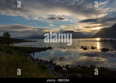 Romantico tramonto del sole di mezzanotte dietro le montagne e il mare sulle isole Lofoten in Norvegia, l'Europa. Prese a nord di Henningsvaer, Vågan, Nordland Foto Stock