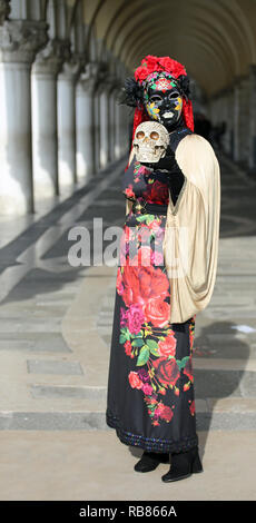 Venezia, VE, Italia - 5 Febbraio 2018: donna mascherata durante il carnevale con un teschio in mano e lo sfondo dei portici del Palazzo Ducale Foto Stock