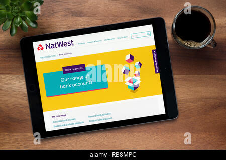 Il sito web di Natwest Bank è visto su un tablet iPad, su di un tavolo di legno lungo con un caffè espresso e una pianta di casa (solo uso editoriale). Foto Stock