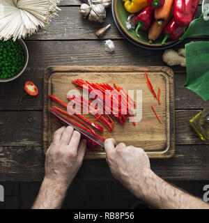 Vista dall'alto le mani maschio preparare vegetariano tagliatelle thai on dark tavolo in legno vista superiore Foto Stock