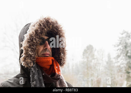 Ritratto di un singolo maschio avventuriero invernali indossando un caldo manto verde con cappa di pelliccia, un blu berretto da sci, un foulard arancione e nero in stile retrò gli occhiali di protezione Foto Stock