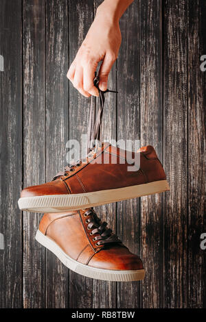 Uomo fashion concept. Mano trattiene per lacci in cuoio marrone scarpe maschio su sfondo scuro Foto Stock