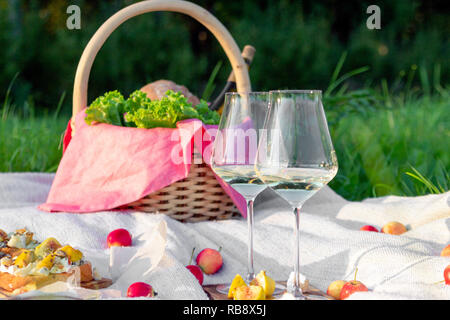 Picnic nella foresta sul prato soleggiato, coperta, cesto di vimini, bicchieri da vino, bruschette con formaggio e pera, spuntini, frutta mele, pane. Concetto di Foto Stock