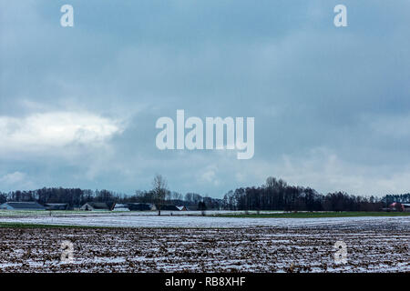 Un po' di neve sul campo arato. Villaggio e la foresta in background. L'inizio dell'inverno in Europa. Foto Stock