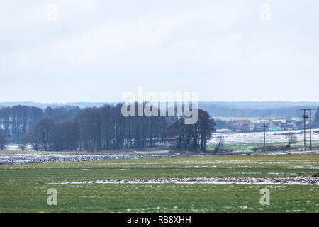 Un po' di neve sul campo arato. Villaggio e la foresta in background. L'inizio dell'inverno in Europa. Foto Stock