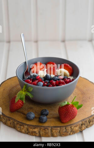 Ciotola con yogurt e frutta fresca come fragole e banane, mirtilli e i semi di melograno su un sfondo rustico Foto Stock