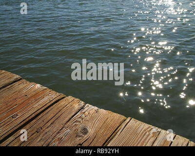 Luce solare scintillante riflessi sull'acqua sotto il bacino di legno. Primo piano delle tavole di legno intemperie. Prospettiva angolata, minimalismo, texture Foto Stock