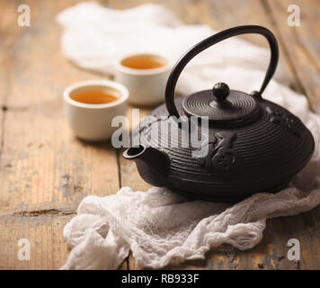 Ancora in vita con tradizionale a base di erbe asiatiche il tè verde preparato in vintage ghisa teiera con organici erbe a secco su tavola in legno rustico. Foto Stock