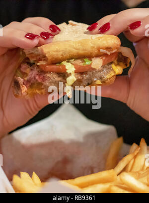 Il cibo da bar: Bar Burger essendo consumato dal patrono. Nessun popolo identifible. La lattuga, pomodoro, formaggio e cipolle fritte visibile. Vista ravvicinata. Foto Stock