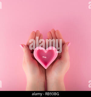 A forma di cuore candela rosa in mani femminili Foto Stock